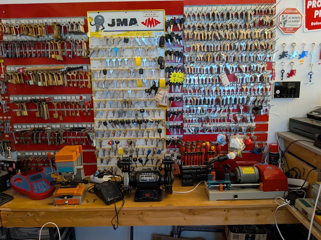 Atelier de serrurerie : présentoirs de bruts de clés et machines de coupe sur un établi.