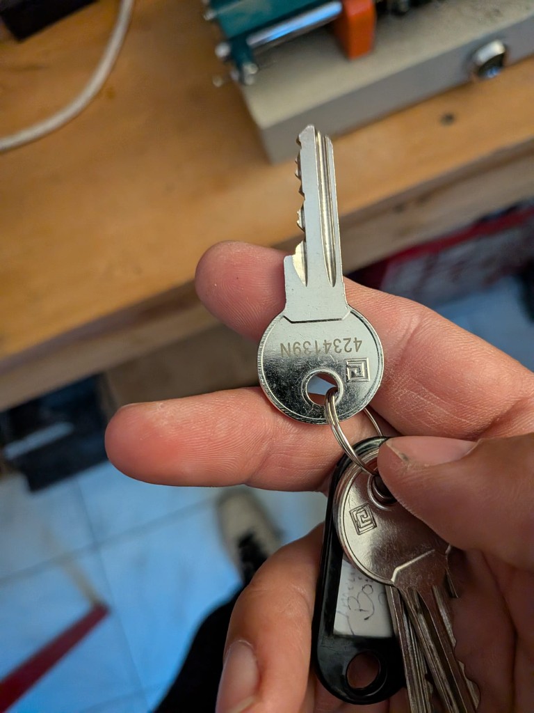 Serrurier tenant un trousseau de clés au-dessus d’un établi, machine de reproduction en arrière-plan.