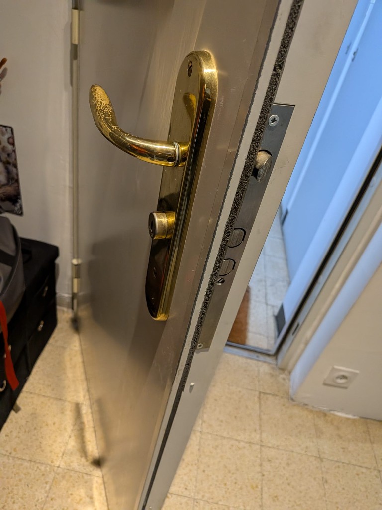 Détail d’une porte claire : mécanisme multipoint sur le chant de la porte et poignée laiton.